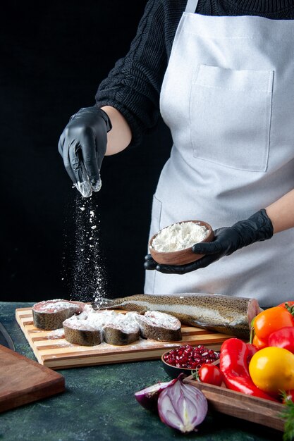 Cuoco unico femminile di vista frontale che copre le fette di pesce crudo con farina sul tavolo da cucina