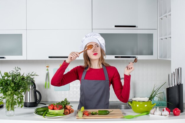 Cuoco unico femminile di vista frontale in cappello del cuoco che mette il cucchiaio di legno davanti al suo occhio