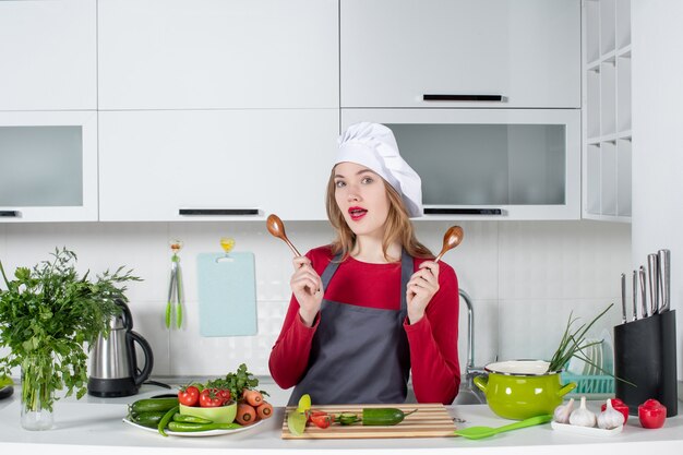 Cuoco unico femminile di vista frontale in grembiule che tiene i cucchiai di legno in cucina