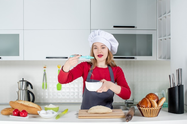 Cuoco unico femminile grazioso di vista frontale in cappello da cuoco e grembiule che sbatte le uova in cucina