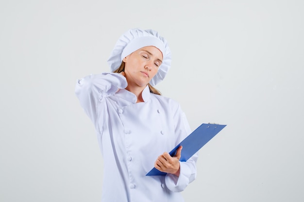 Cuoco unico femminile in appunti della holding dell'uniforme bianca con la mano sul collo e che sembra stanco