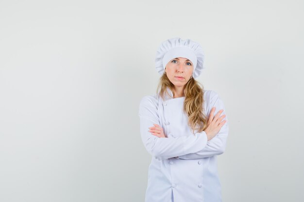 Cuoco unico femminile in piedi con le braccia incrociate in uniforme bianca e dall'aspetto serio.