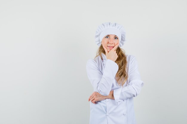 Cuoco unico femminile in uniforme bianca che sta nella posa di pensiero e che sembra ragionevole