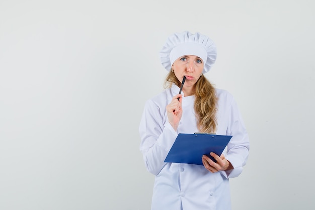 Cuoco unico femminile in uniforme bianca che tiene appunti e penna e sembra pensieroso