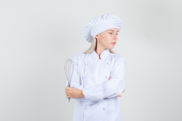 Cuoco unico femminile in uniforme bianca che tiene frusta e che osserva da parte