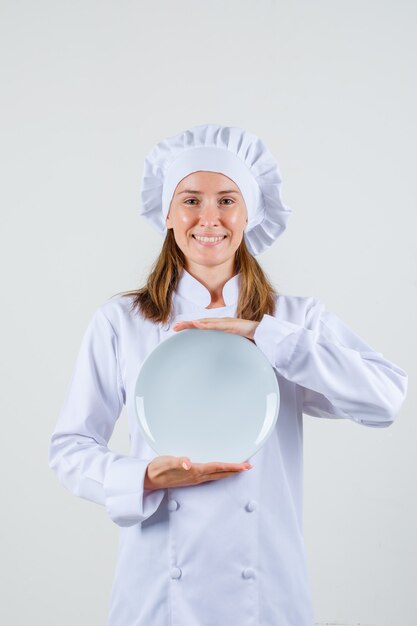 Cuoco unico femminile in uniforme bianca che tiene piatto vuoto e che sembra felice.