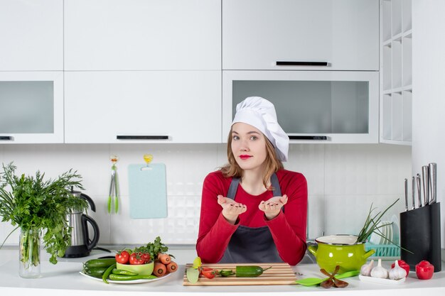 Cuoco unico femminile sveglio di vista frontale in cappello del cuoco che sta nella cucina