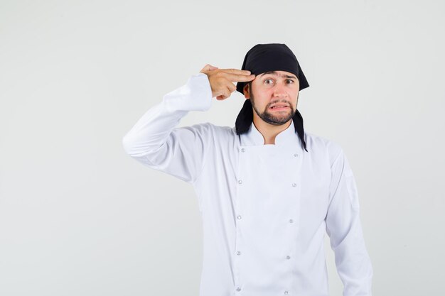 Cuoco unico maschio che fa gesto di suicidio in uniforme bianca e sembra ansioso. vista frontale.
