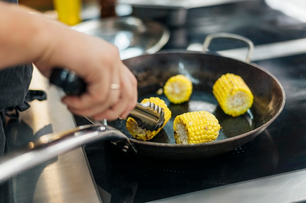 Cuoco unico maschio che frigge le pannocchie di mais in padella