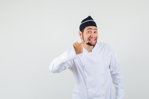 Cuoco unico maschio che mostra i suoi denti in uniforme bianca e che sembra carino, vista frontale.