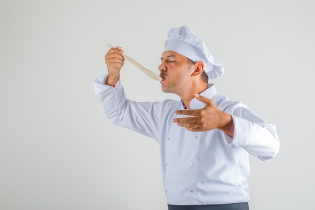 Cuoco unico maschio che prova pasto in uniforme, grembiule e cappello e che sembra sicuro