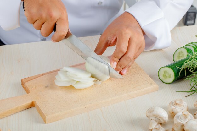 Cuoco unico maschio che taglia cipolla a pezzi sul tagliere in cucina in uniforme
