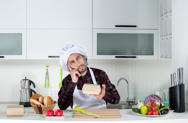 Cuoco unico maschio di pensiero di vista frontale che tiene scatola di hamburger in cucina