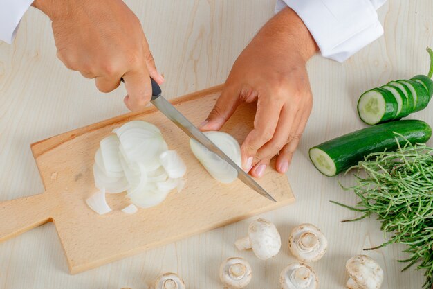 Cuoco unico maschio in uniforme che taglia cipolla a pezzi sul tagliere in cucina