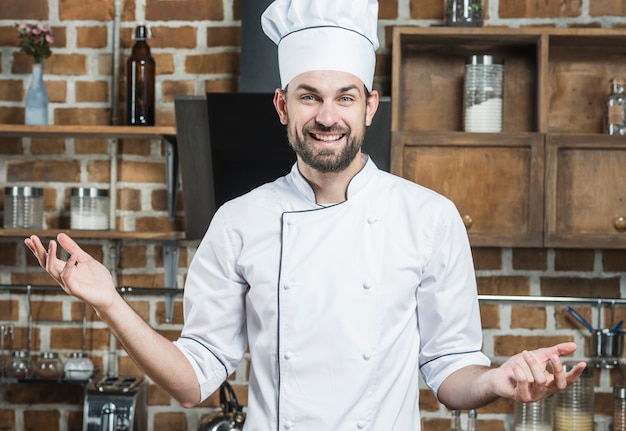 Cuoco unico maschio sorridente che sta nella scrollata delle spalle della cucina