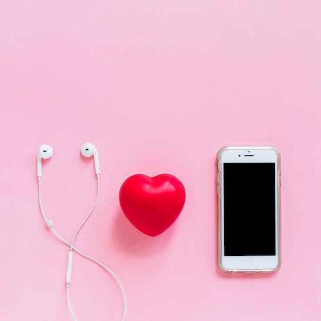 Cuore rosso; auricolare e smartphone su sfondo rosa