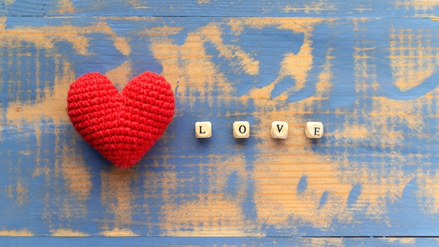 Cuore rosso lavorato a maglia a mano con lettere in legno che compongono la parola amore. Vista dall'alto