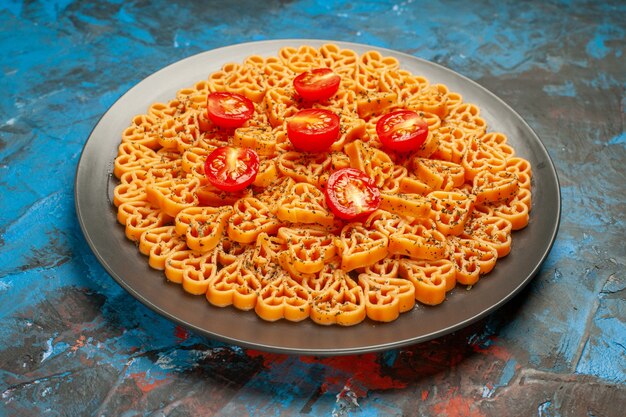 Cuori di pasta italiana vista dal basso tagliati pomodorini su piatto ovale nero su superficie blu scuro