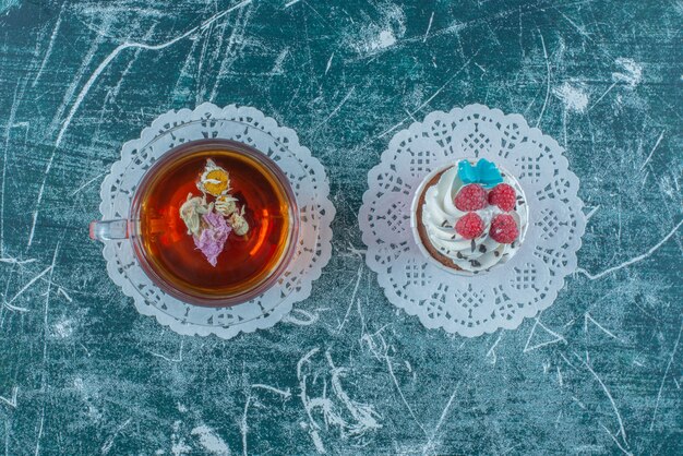 Cupcake ricoperto di crema e una tazza di tè su sfondo blu. Foto di alta qualità