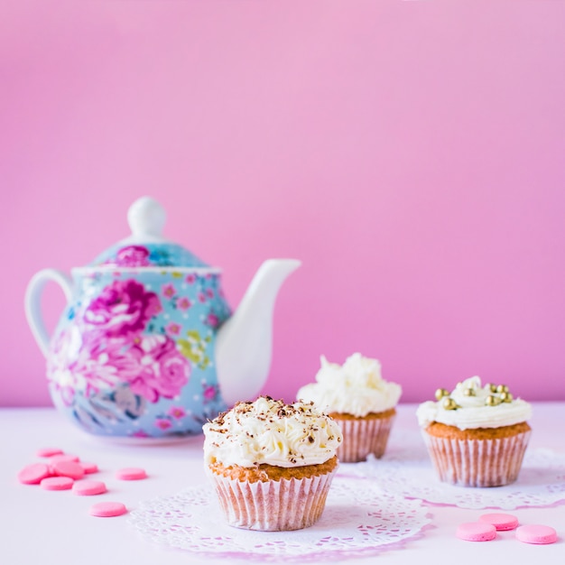 Cupcakes; caramelle e teiera su superficie bianca