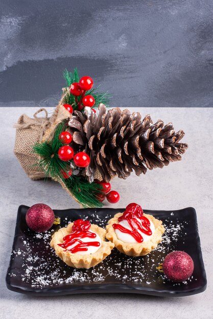Cupcakes con salsa di fragole su un piatto nero, impacchettato con ornamenti natalizi sulla superficie di marmo