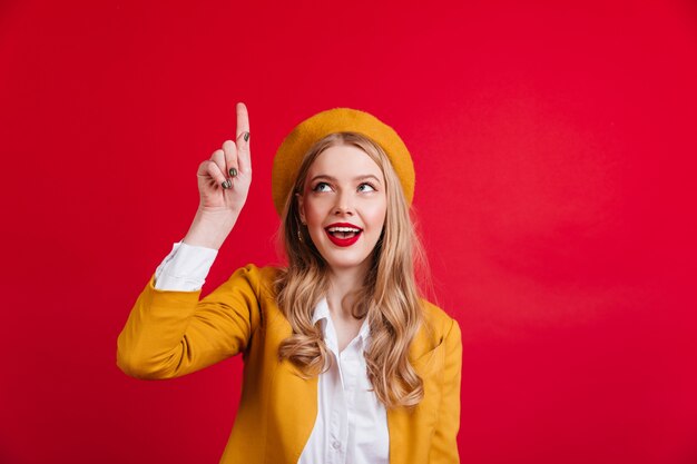 Curiosa donna francese che punta il dito verso l'alto. raffinata ragazza alla moda in berretto giallo.