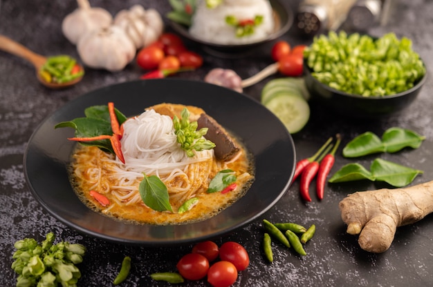 Curry di pollo in una tazza nera con spaghetti di riso.