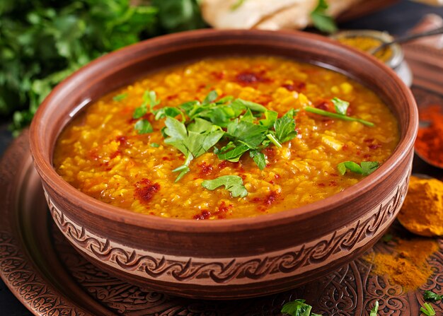 Curry piccante indiano Dhal in ciotola, spezie, erbe, tavola di legno nera rustica.