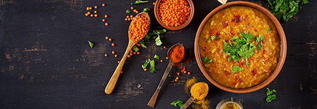 Curry piccante indiano Dhal in ciotola, spezie, erbe, tavola di legno nera rustica.