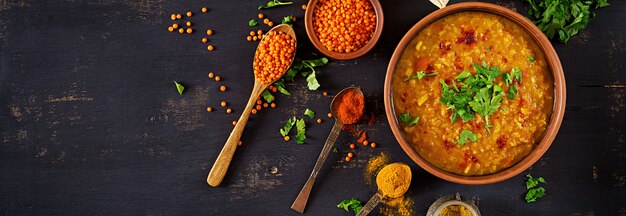 Curry piccante indiano Dhal in ciotola, spezie, erbe, tavola di legno nera rustica.