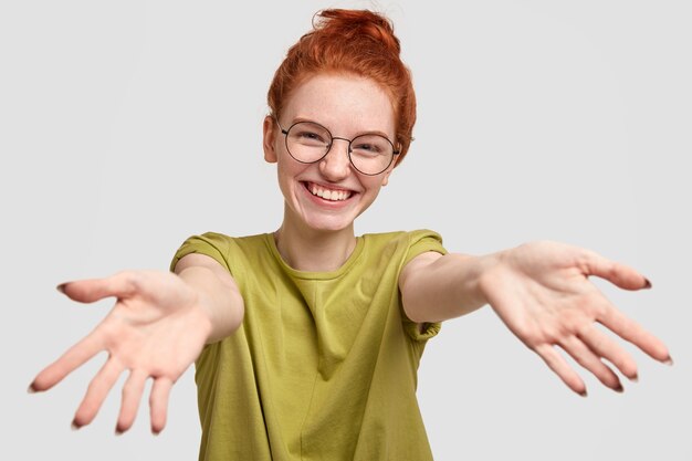 Da quanto tempo non ti vedo! Gioiosa ragazza dai capelli rossi carina dà un caldo abbraccio, tira le mani, saluta il migliore amico, sorride ampiamente, modella contro il muro bianco, esprime buoni sentimenti.