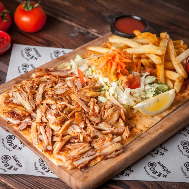 Da sopra pezzi di pollo fritto con limone e patatine fritte e insalata nel piatto di legno