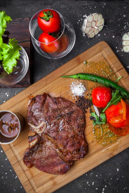 Dall'alto bistecca con pomodoro e carta nel tagliere