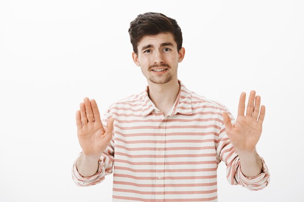 Dammi una pausa, non voglio problemi. Studente maschio bello infastidito e infastidito con espressione dispiaciuta, tirando i palmi verso il gesto di no o stop, in piedi deluso sul muro grigio