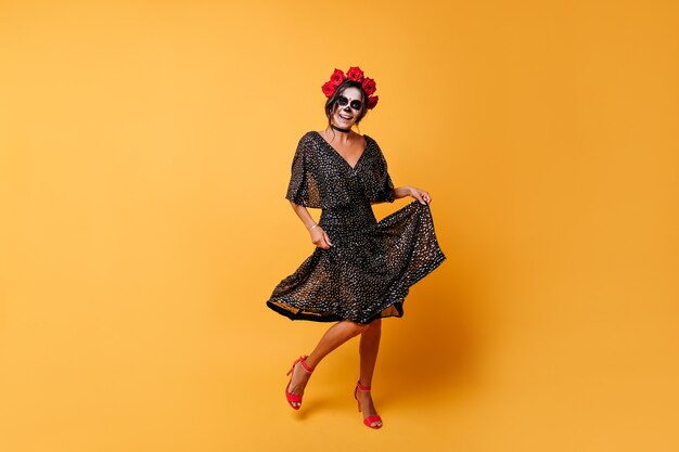Dancing attivo modello messicano in posa su sfondo arancione. Ritratto integrale della ragazza che si rallegra di Halloween.