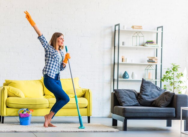 Dancing sorridente della giovane donna nel salone con le attrezzature di pulizia