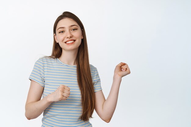 Danza ragazza caucasica sorridente, guardando felice a porte chiuse. La giovane donna muove le sue mani. sta su bianco.