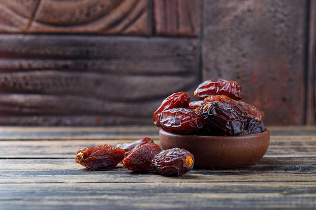 Date dolci in un piatto di argilla su piastrelle di pietra e fondo in legno