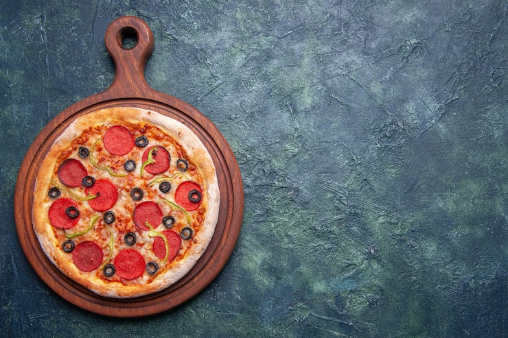 Foto gratuito delicia pizza su tavola da taglio in legno sul lato destro su superficie blu scuro con spazio libero