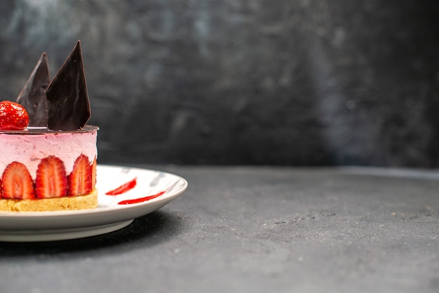 Deliziosa cheesecake vista frontale con fragole e cioccolato su piatto ovale su spazio libero scuro