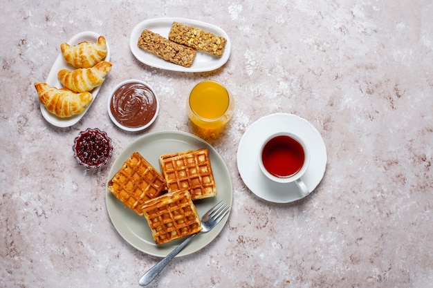 Deliziosa colazione con caffè, succo d'arancia, waffle, cornetti, marmellata, pasta di noci alla luce, vista dall'alto