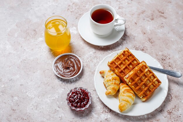 Deliziosa colazione con caffè, succo d'arancia, waffle, cornetti, marmellata, pasta di noci alla luce, vista dall'alto