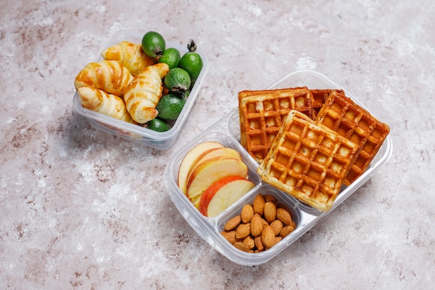 Deliziosa colazione con mandorle, fette di mele rosse, waffle, cornetti su scatola di plastica per il pranzo alla luce