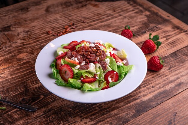 Deliziosa insalata di fragole con lattuga verde e carne in un piatto bianco