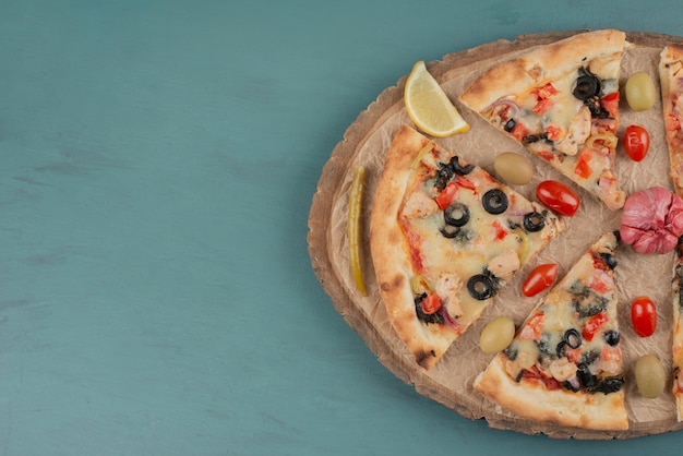 Deliziosa pizza calda con olive e pomodori sulla superficie blu.