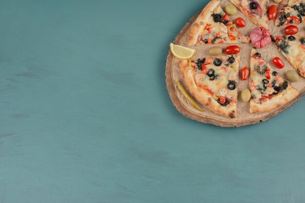 Deliziosa pizza calda con olive e pomodori sulla superficie blu.