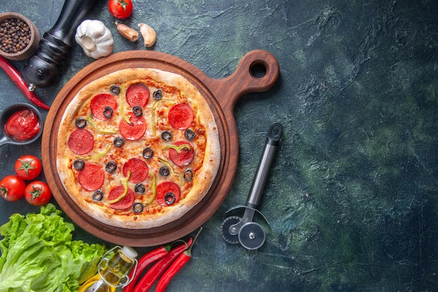 Deliziosa pizza fatta in casa su tagliere di legno pomodori ketchup aglio verde bottiglia di olio sul lato destro su superficie scura
