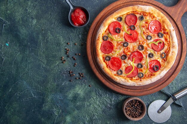 Deliziosa pizza su tagliere di legno e ketchup di pepe su superficie scura isolata in primo piano