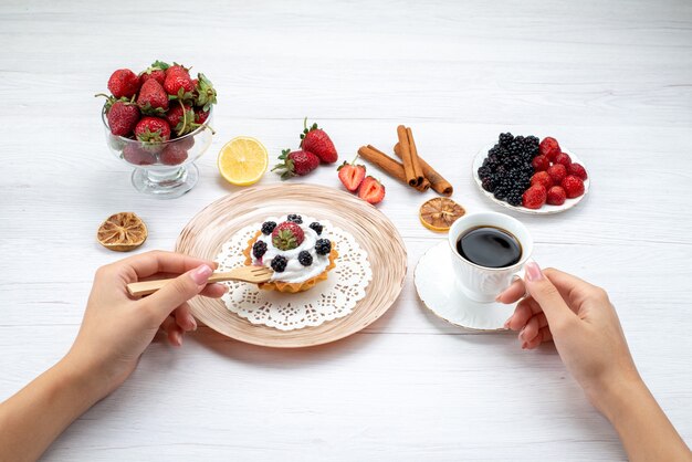 deliziosa torta cremosa con frutti di bosco che viene mangiata da una donna con caffè alla cannella sulla scrivania bianca chiara, torta dolce foto a colori