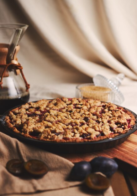 Deliziosa torta di prugne con caffè Chemex e ingredienti con tessuto su un tavolo in legno con tessuto